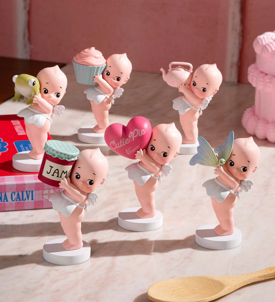 Set of baby-themed figurines on a wooden surface with a pink background