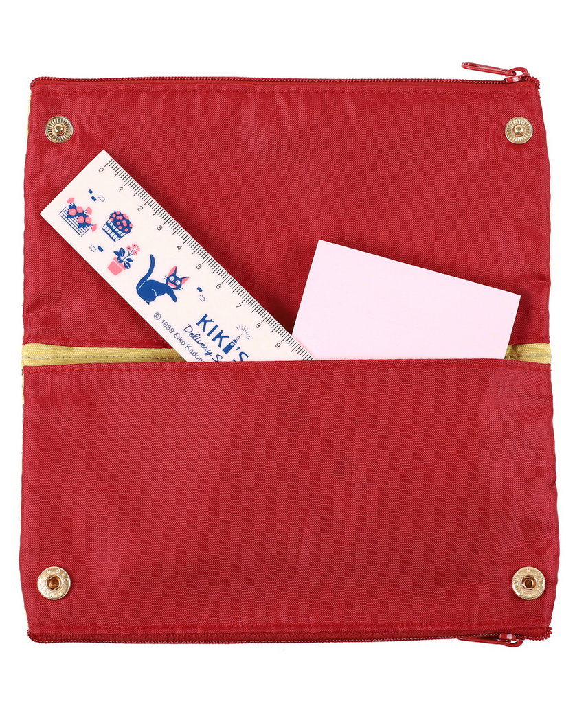 Interior view of the Kiki's Delivery Service Pen case unsnapped and opened flat showing the brick red lining and pockets holding a ruler and note pad. 