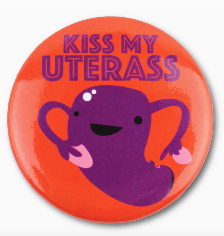 Round magnet with illustrated purple uterus on a red background. With "Kiss My UterAss" written in purple letters.