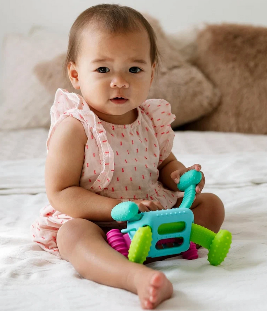A baby sitting on a bed playing with the Knudll Sensory Activity Toy