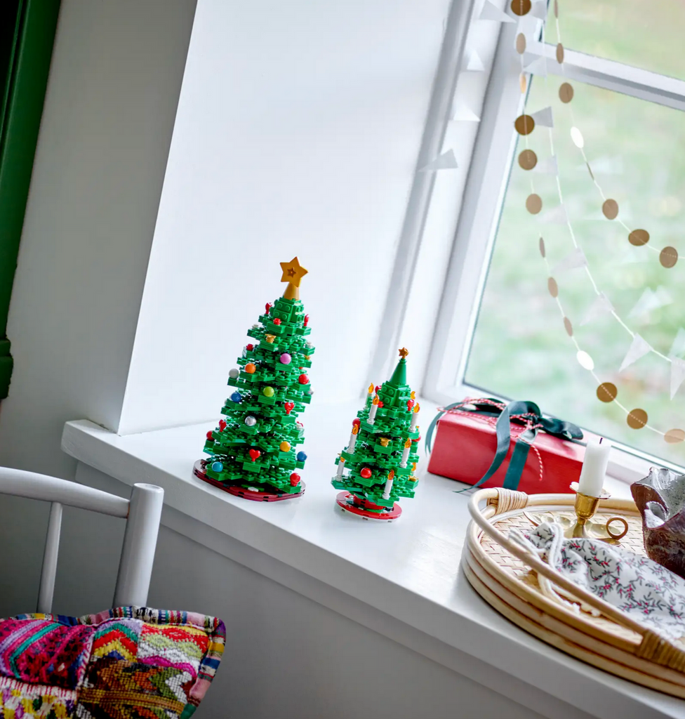 Each of the LEGO Christmas Trees from the 2 in 1 LEGO Christmas Tree set, in a window sill with other festive decorations. 