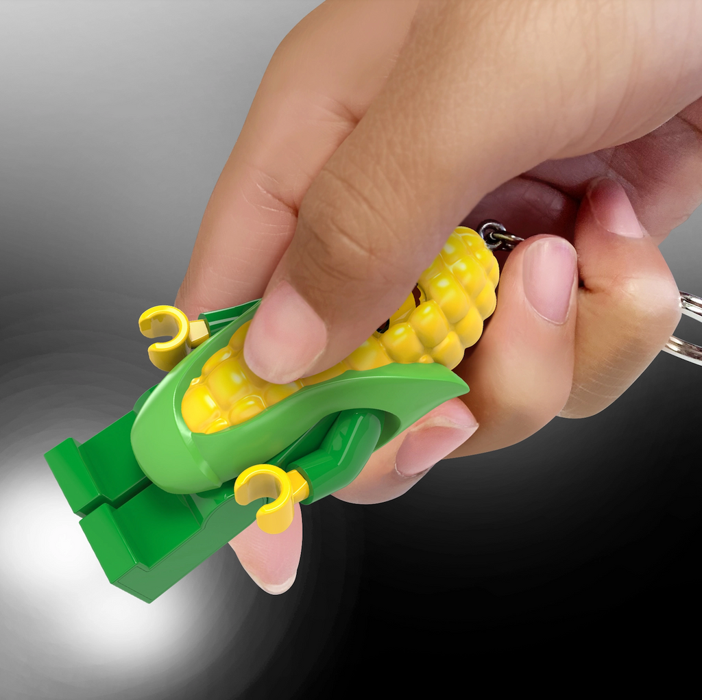 LEGO minifigure Corn Cob Guy keyring, held in a hand which is squeezing it to shine both the lights in it's feet. 