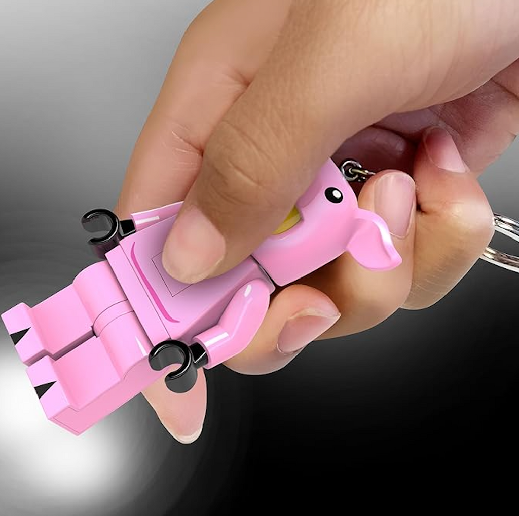 The LEGO LED minifigure Piggy Girl keychain being squeezed on to activate the lights that shine from the bottom of her feet. 