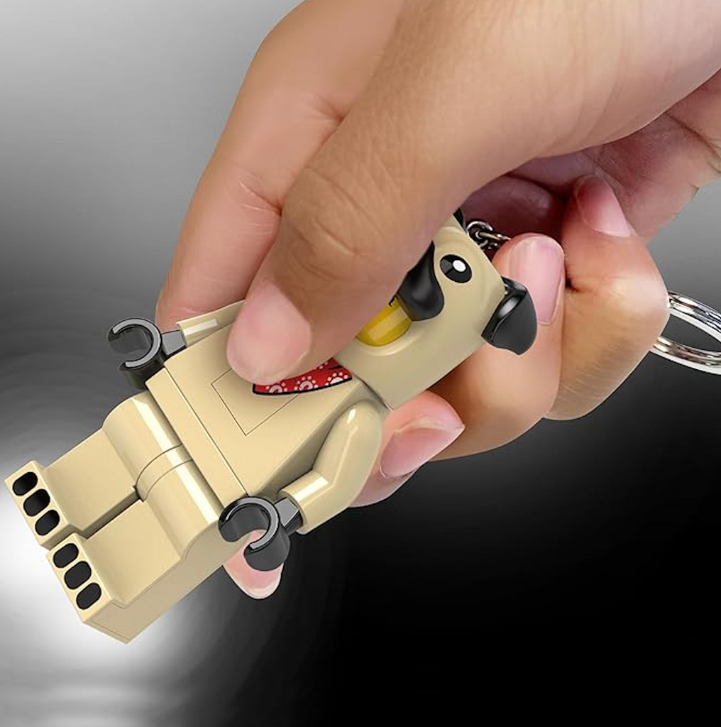 The LEGO LED Pug Guy Keychain being held and squeezed to turn on the flashlight that shines from both feet. 