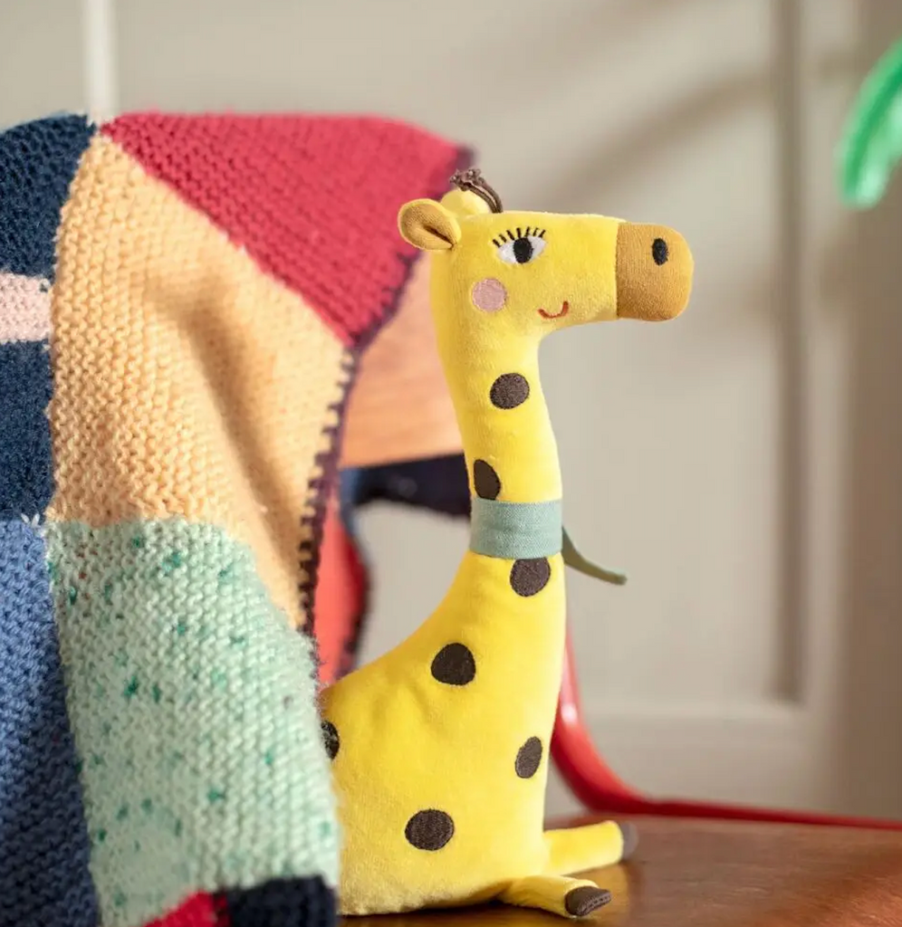 Les Toupitis Giraffe rattle resting on a colorful blanket. 