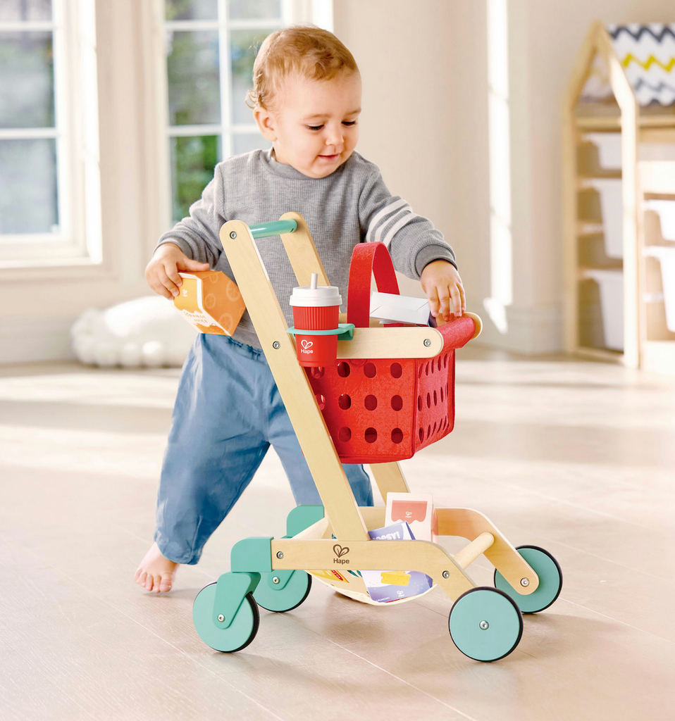 A toddler putting toys in the Little Shopper Cart and Basket. 