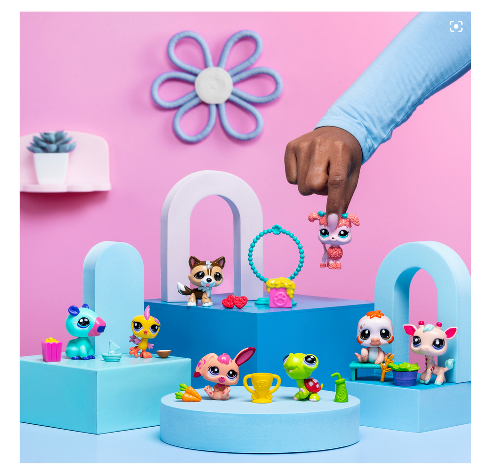 Child's hand picking up one of the various Littlest Pet Shop Pet Pairs that are displayed on a blue and pink table.