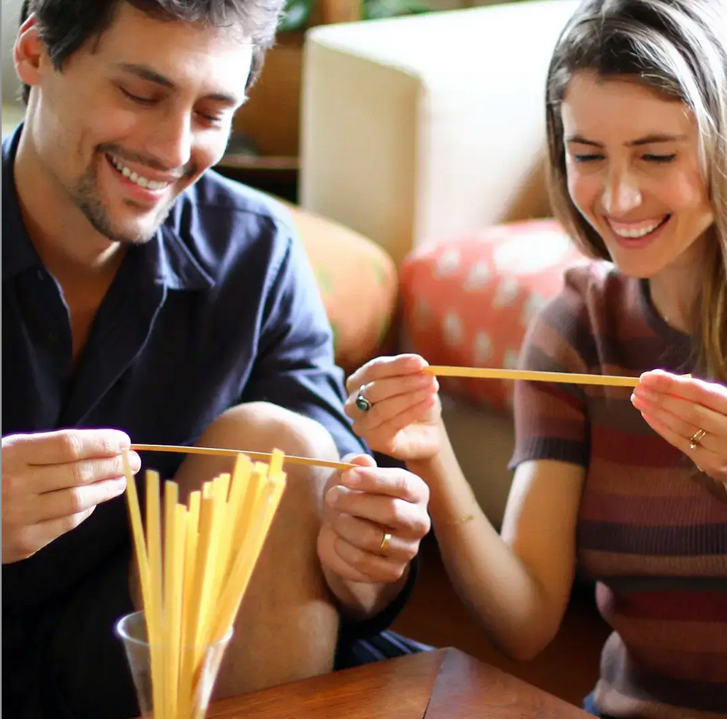 A couple sitting together at a table and each holding a stick with a question on it from the Love Language Conversation game. 