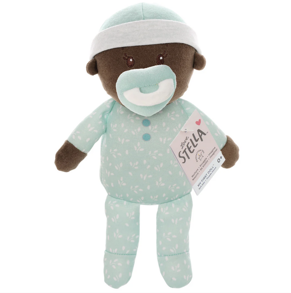 Plush, Love,Stella baby doll with brown skin tone in a standing position with the magnetic pacifier in it's mouth. 