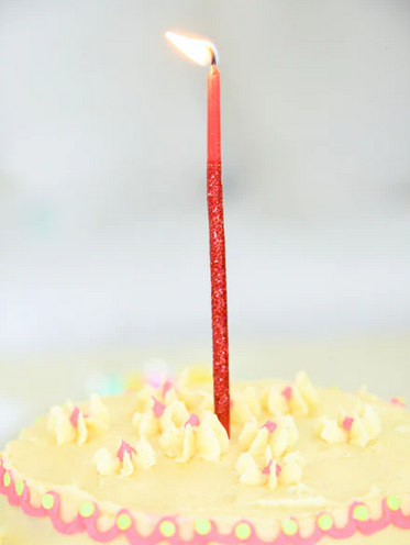 The Lucky Token Red Candle lit and on top of a  cake with yellow frosting. 