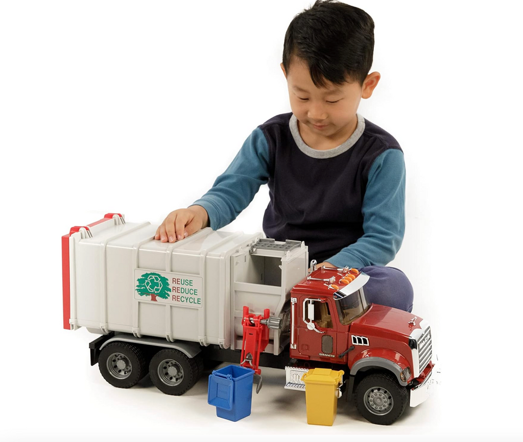 A kid sitting on the floor and playing with the big Mack Granite Side Loading Garbage Truck by Bruder. 