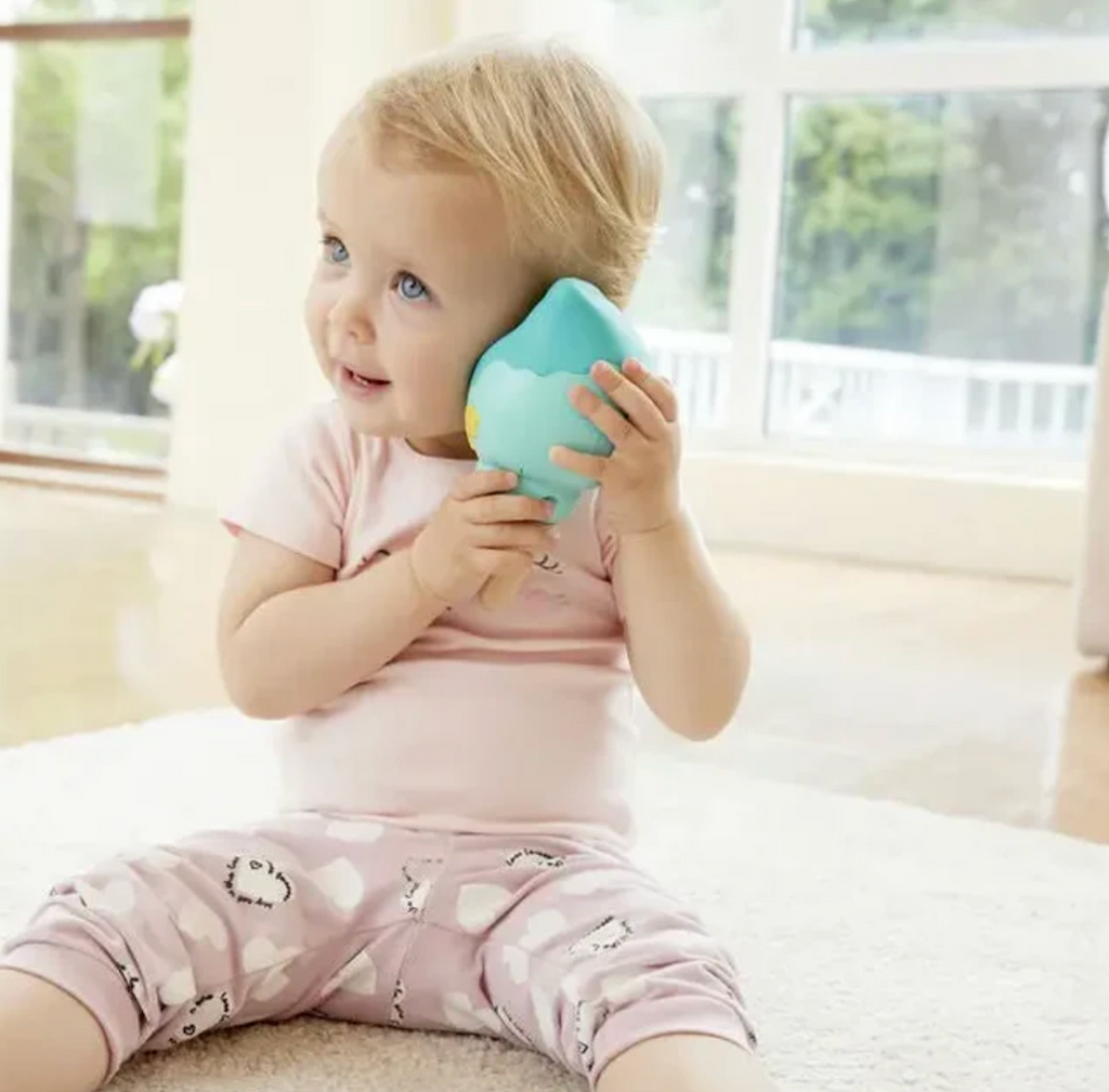 A toddler with the Magic Music Conch toy holding it up to her ear and listening to music and sounds. 