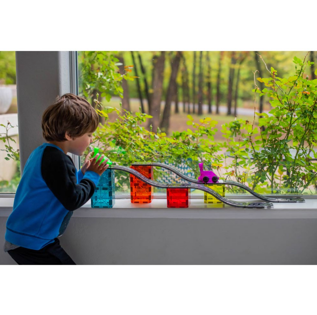 Child playing with the Magna-tiles downhill duo racing set in front of a window with greenery outside.