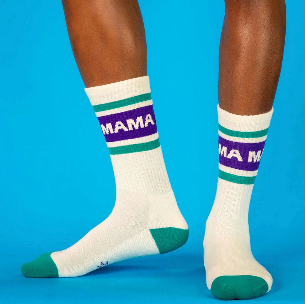 White socks with purple and green stripes that read 'MAMA' being worn by an adult. 