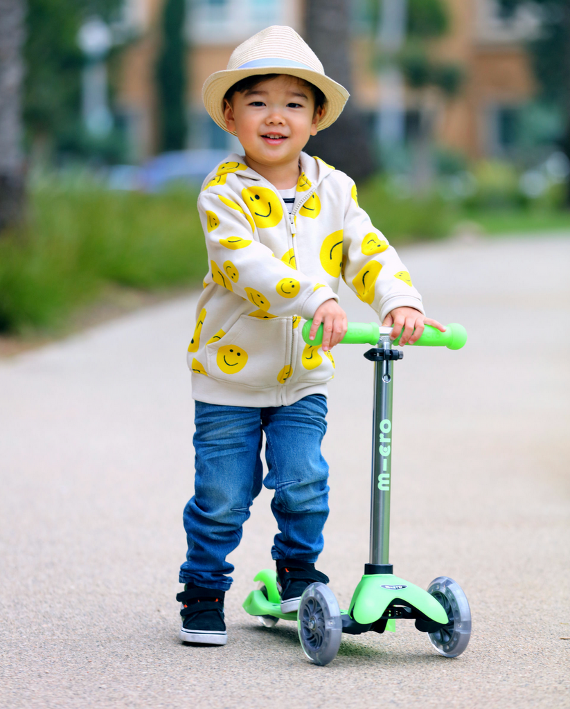 A little guy riding the Micro Mini Glow Plus LED Scooter in Icy Lime. 