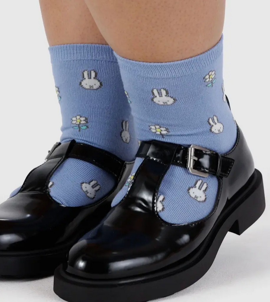 The blue Miffy crew socks on a pair of feet wearing a pair of black Mary Jane shoes. 