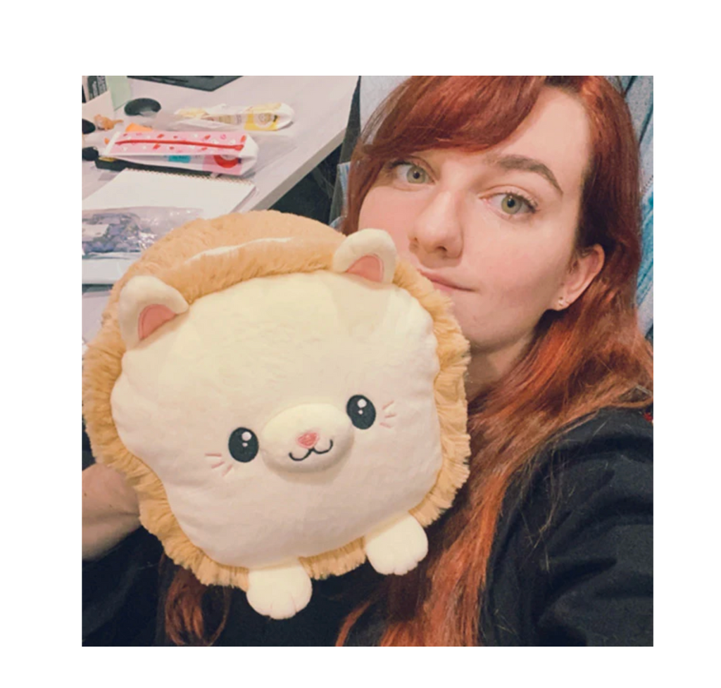 Red haired woman in a green shirt holding the Squishable Mini Cat Loaf plush.