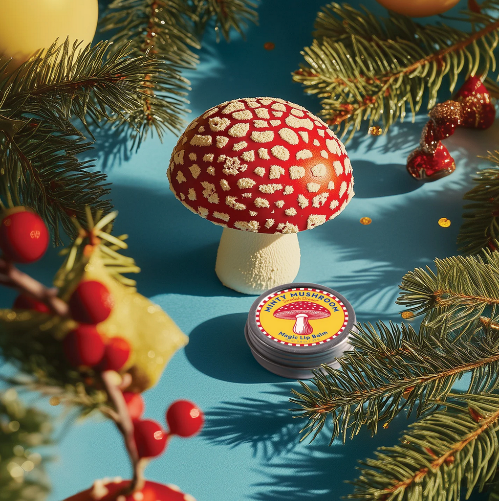 Minty Mushroom Magic Lip Balm tin nestled amongst green foilage and red mushrooms.