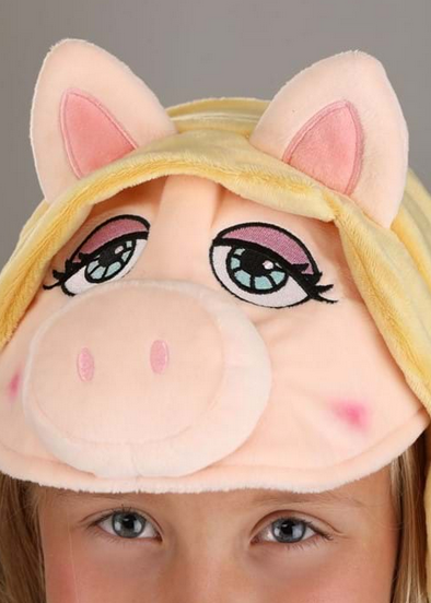 The Miss Piggy is a a fabric-covered headband. Plush fabric makes up the three-dimensional face, which includes attached hair and a pair of ears. Piggy's eyes are embroidered on the front right above the stuffed snout. Shown here being worn by a child. 