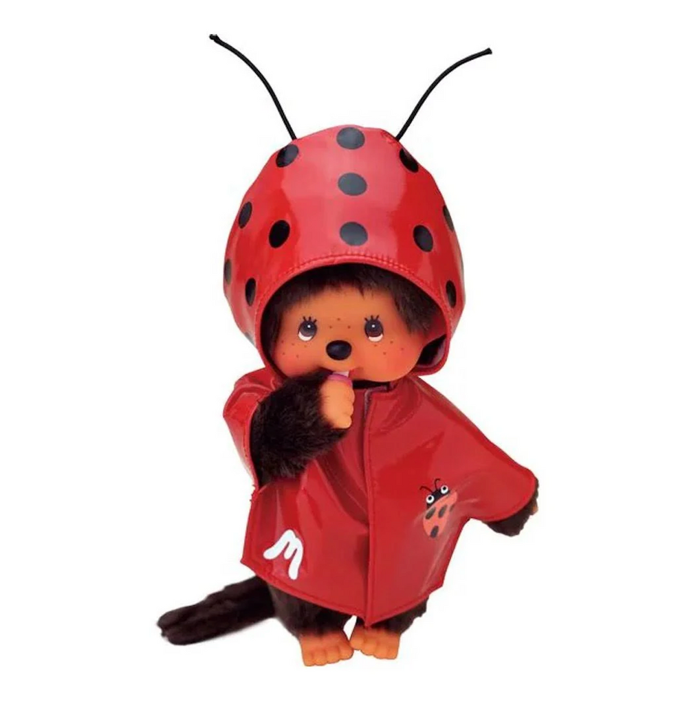 The Monchhichi doll in a standing pose and facing forward wearing the ladybug raincoat with antennae sticking up. 