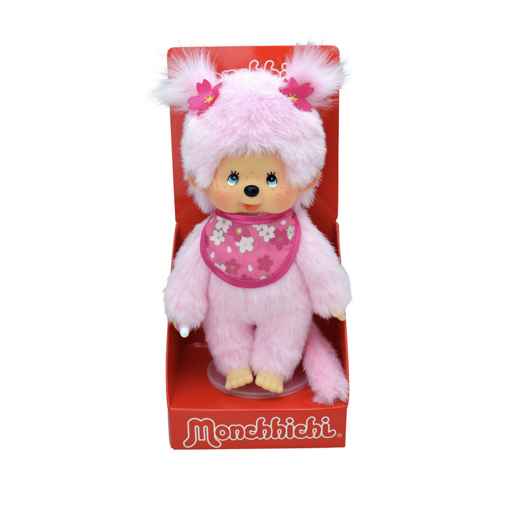 Light pink plush Monchhchi doll wearing a bib with pink Sakura blossoms. Packaged in an open red box. 