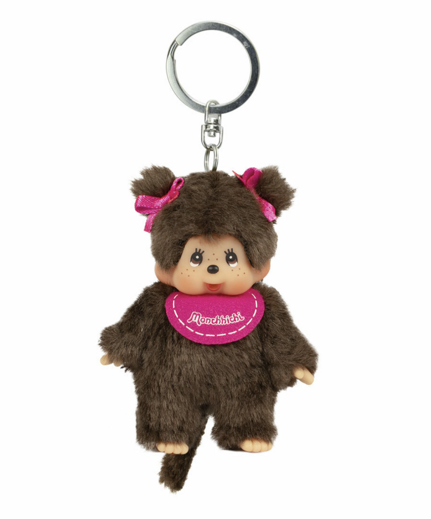 Monchhichi mini plush doll wearing a pink bib and pink ribbons in her pigtails. Attached to a round, silver key ring. 