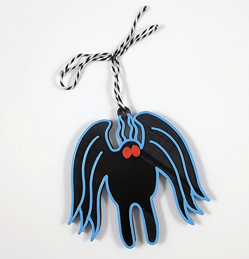 3D printed Mothman ornament. Mothman has a black body outlined in blue with red eyes. The ornament is hanging from white and black striped yarn. 