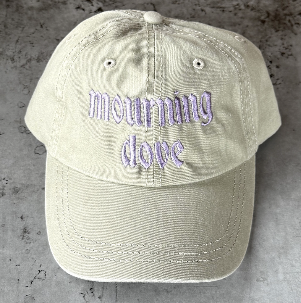Light gray ball cap with "mourning dove" embroidered on the front in light purple. 