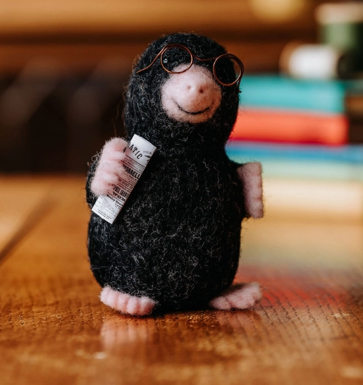 Close up view of felted Mister Mole holding a newspaper, and wearing his wire rimmed glasses. 