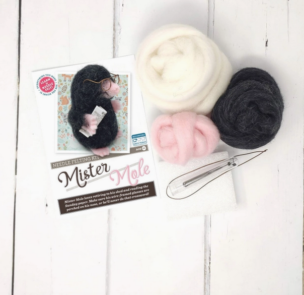 The instruction booklet, needles, felting tool and wool in white, pink, and slate gray included in the Mister Mole Needle Felting Craft Kit. 
