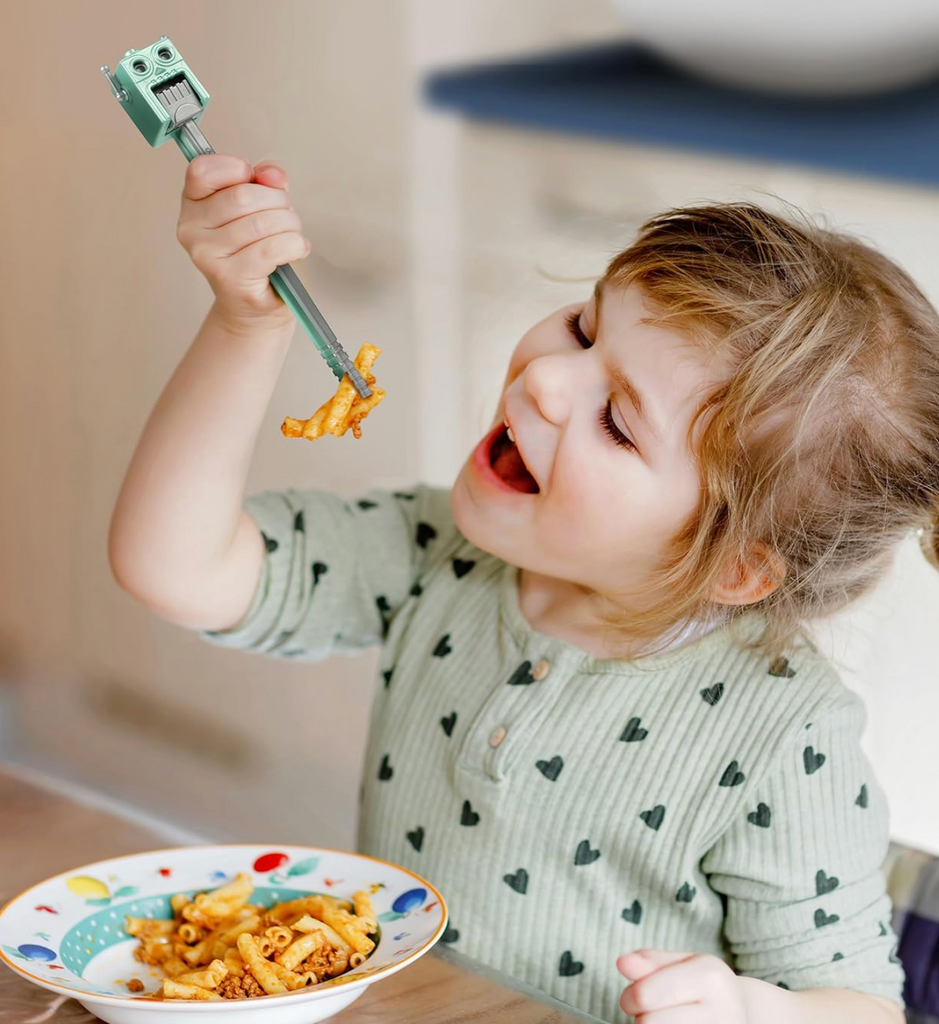 A young child using the Robot chopsticks to eat pasta. 