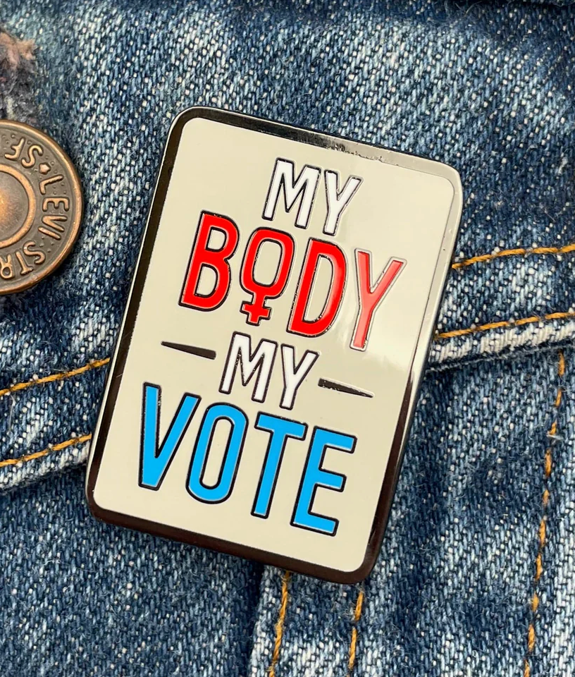 Enamel pin attached to a jean jacket that reads "My Body My Vote"