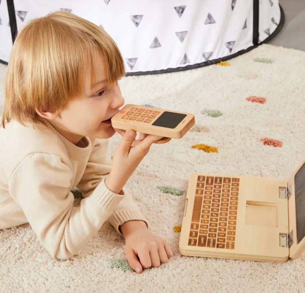 A child talking into the wooden toy My Own Cell Phone while lying on the floor. 