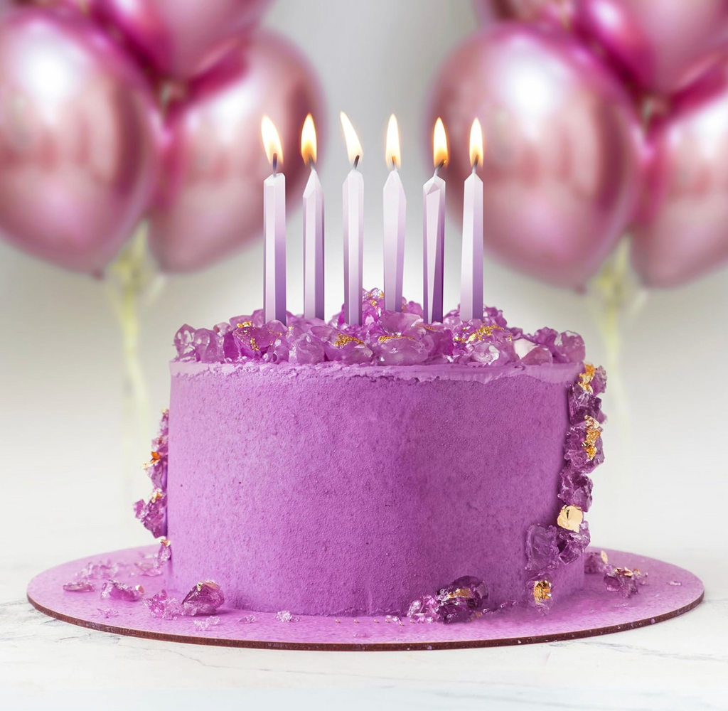 Purple cake with gold and purple decorations with the Mystic Wicks candles lit on the top. 