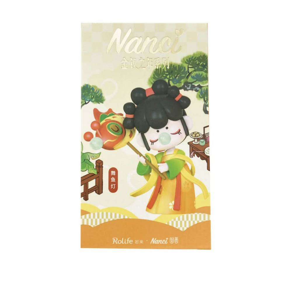 A box with an illustration of one of the Nanci Blooming Girl collectible figures. This Nanci is wearing a yellow robe with green sleeves and yellow and orange scarves, she is holding a stick with a colorful dragon head at the top. 