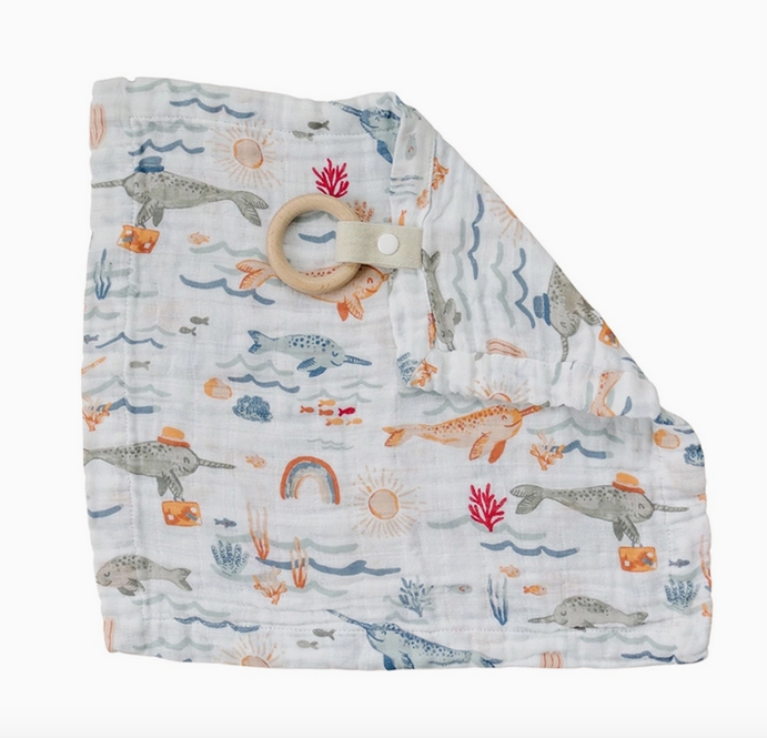 Narwhal Muslin Teether blanket laid flat with the teething ring. The Narwhal print has narwhals swimming amongst sea plants and rainbows.