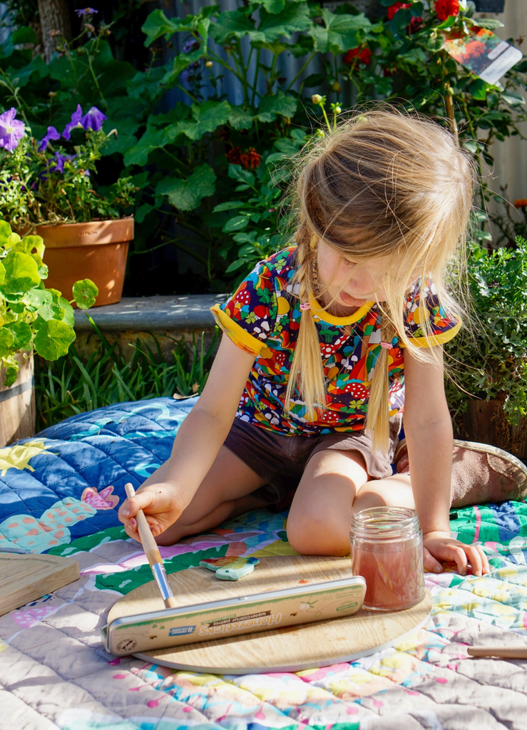 Child sitting outside on a blanket painting with watercolors.