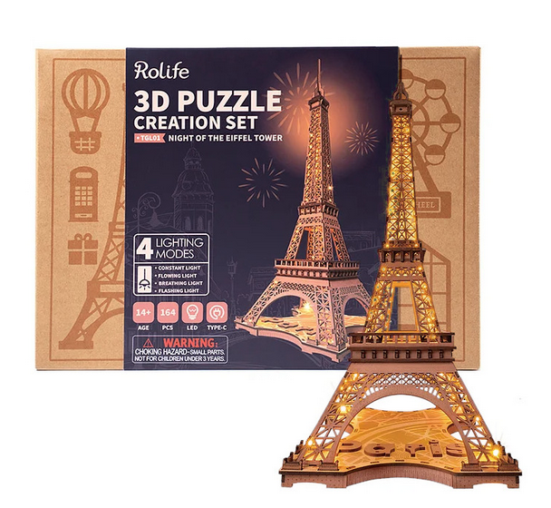 Box for the Night of the Eiffel Tower 3D wooden puzzle, with a completed puzzle standing in front of it. The box has a printed picture of the completed puzzle.