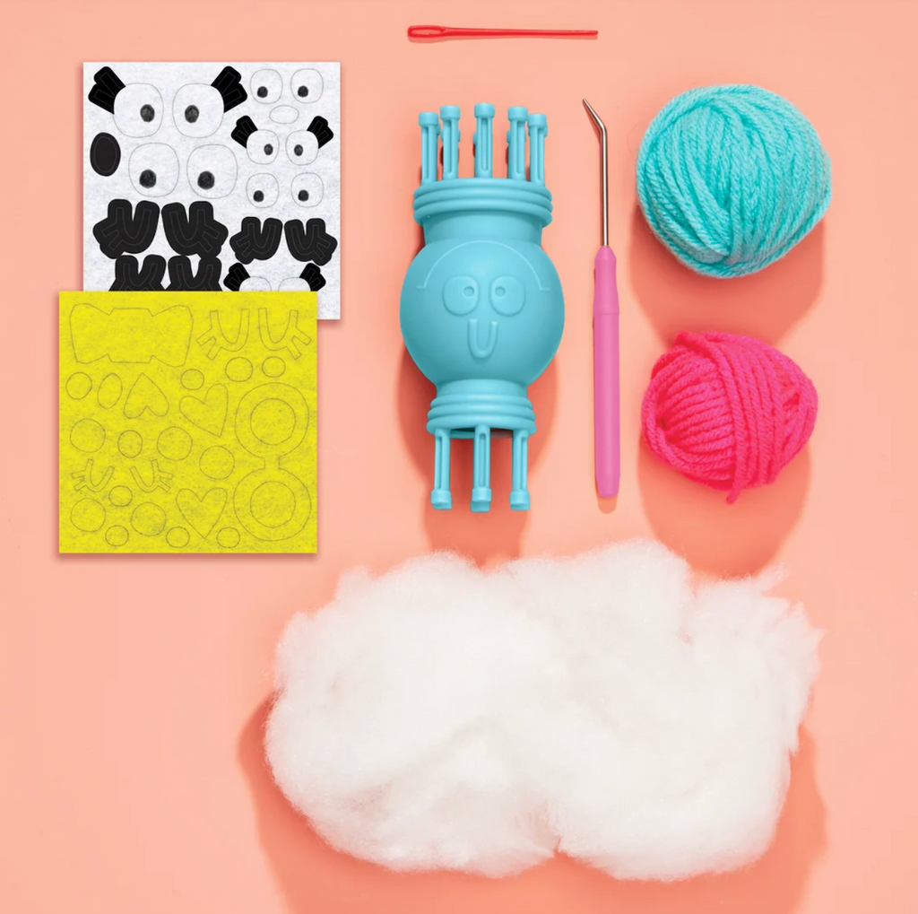 Supplies from the Nimble Knitter Flipper craft kit including yarn in pink and blue, cotton stuffing, plastic needle, stickers and the nimble knitter tool. 
