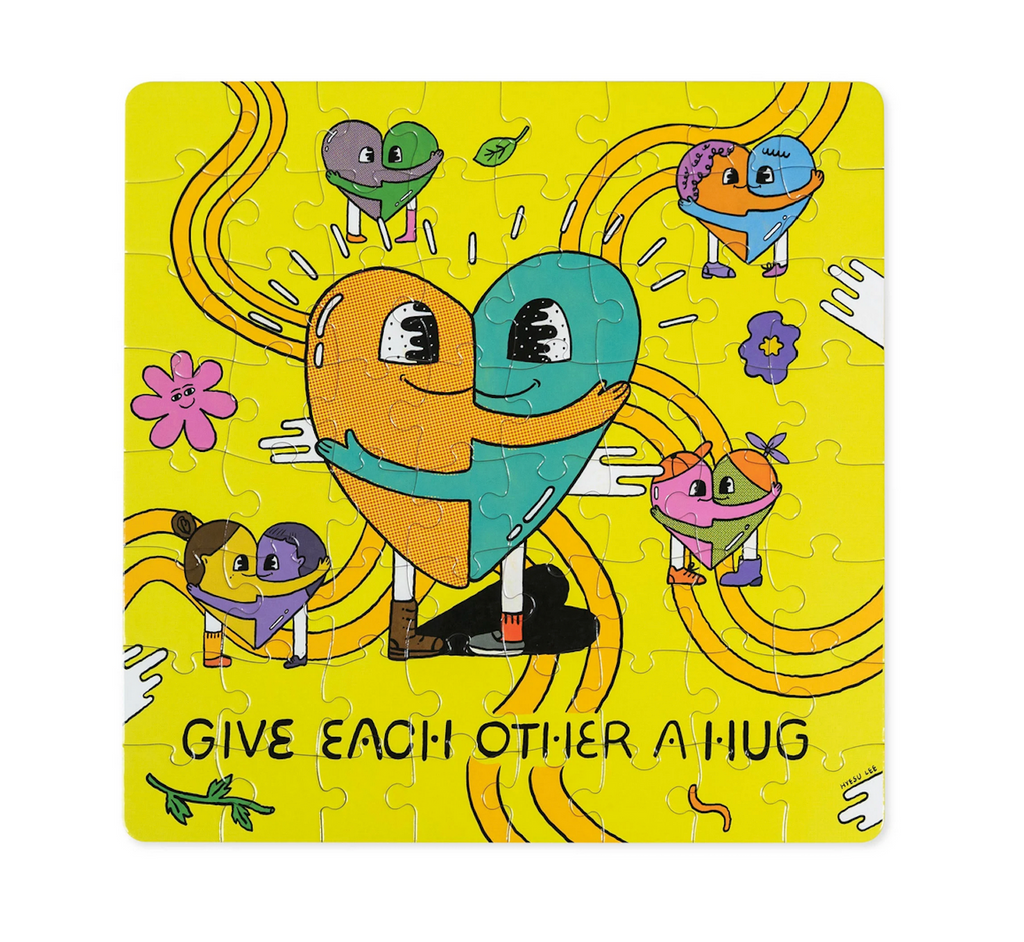 The completed puzzle with artwork by Hyesu Lee. The final image shows yellow and green characters embraced in a hug in the center with other groups of characters hugging to form hearts throughout. At the bottom of the puzzle there is text that reads "Give Each Other A Hug 