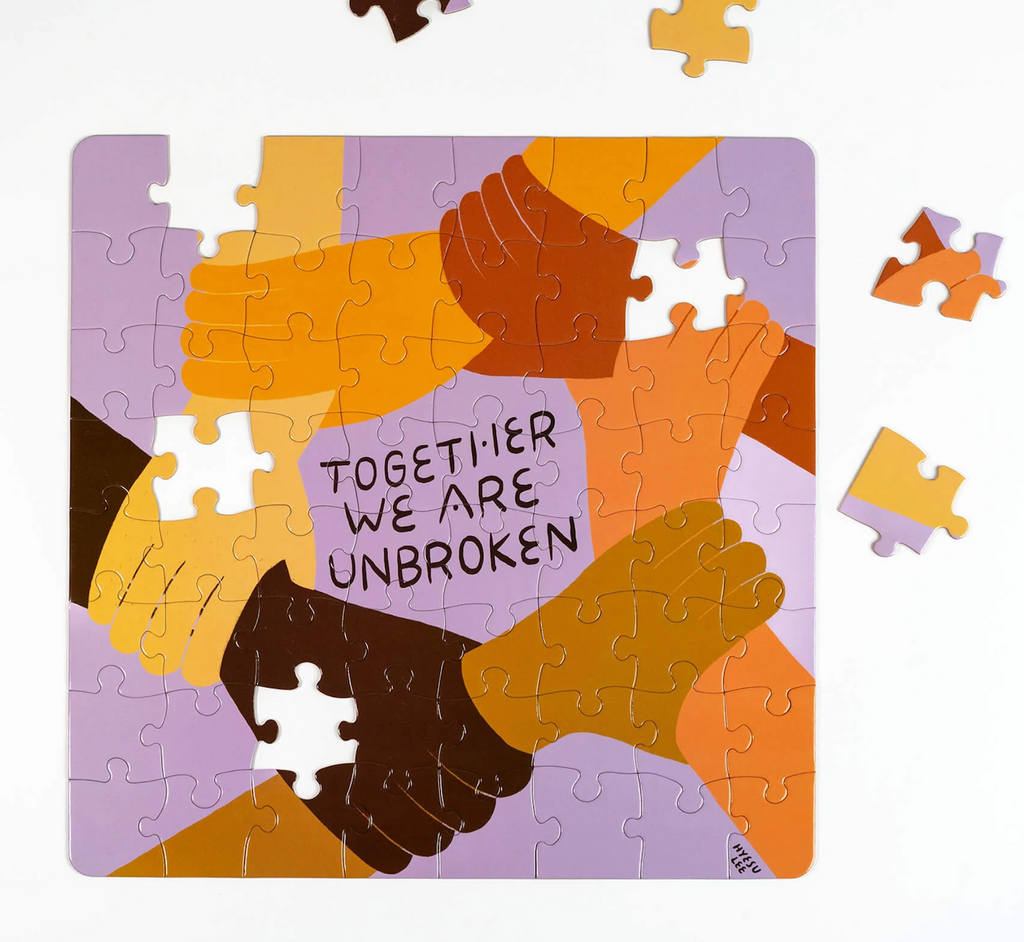 The Unbroken puzzle near completion with an image of multiple skin toned hands clasped together to form a circle with text that reads "Together We Are Unbroken" in the center. 
