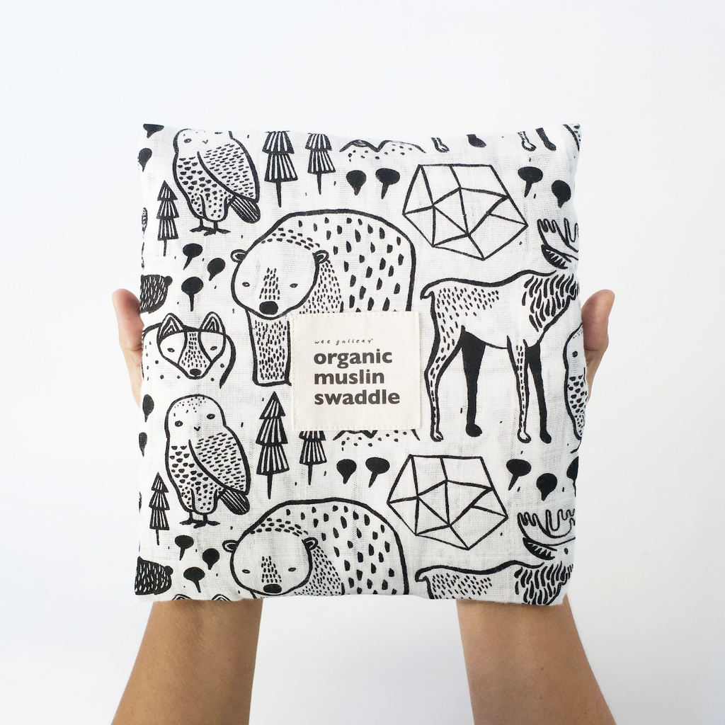 The Nordic Organic Muslin Swaddle folded into a square with a label on the front. The blanket has an black and white animal print. 