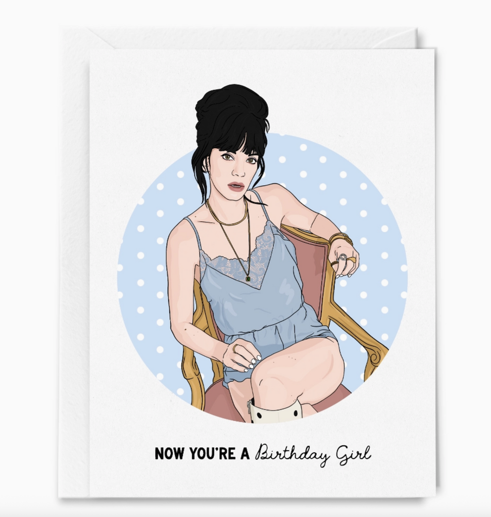 An illustrated greeting card with a young lady in a blue jumper sitting in a chair that reads "Now You're a Birthday Girl" 