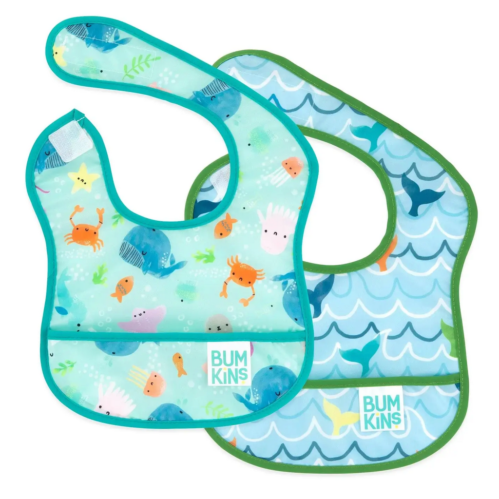 Two baby bibs with ocean-themed design. Whales, octopus, crabs and other marine life on a blue/green background and another with whale tails floating on waves on a blue background. Both have pockets on the bottom to catch food and spills. 