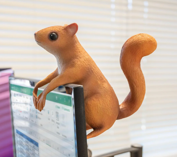The Office Squirrel is an 8-1/2" tall, stuffed latex squirrel with bendable, posable arms hanging on a computer screen. 