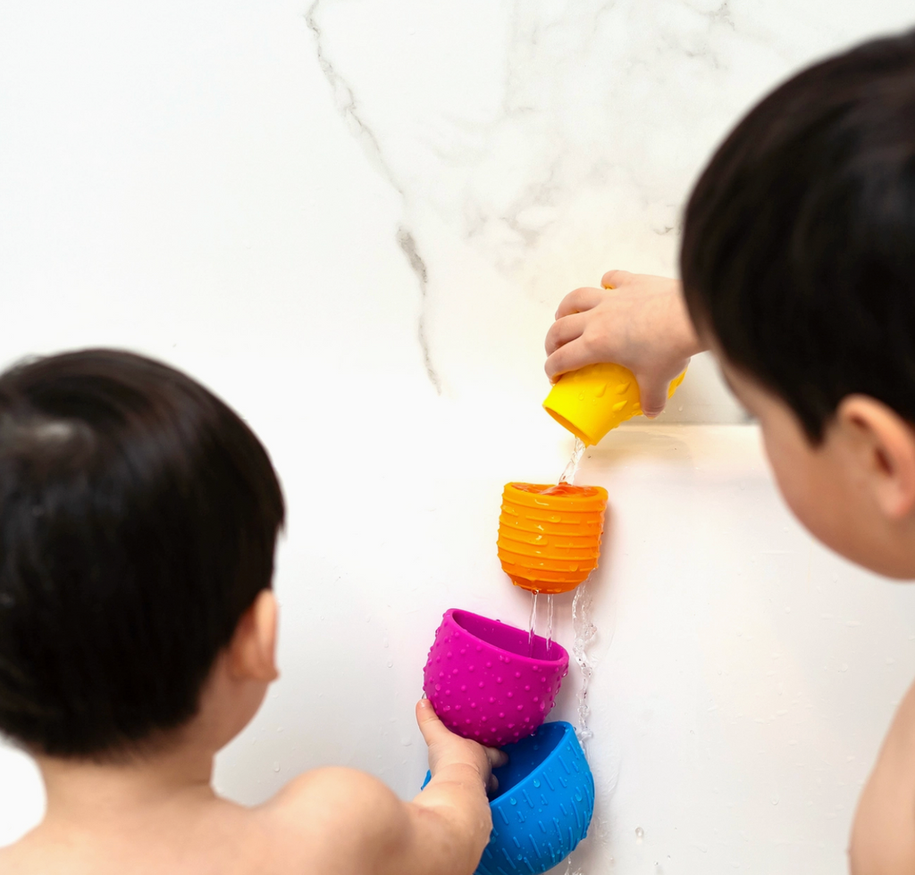 Back view of of two children playing with Oomplz in the tub.