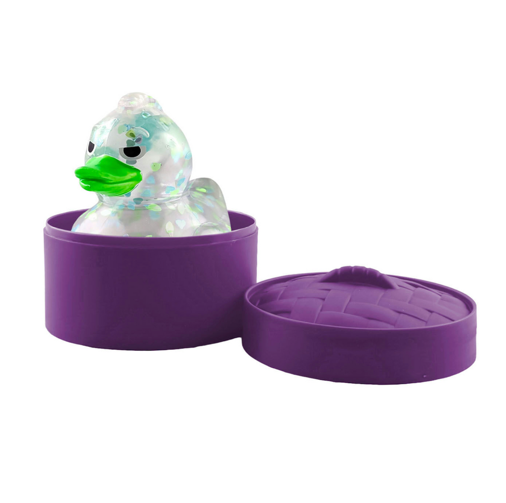 A clear duck squishy with a bright green beak sitting inside a purple steamer basket. 