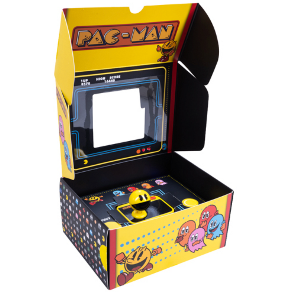 Pac Man Plug and Play mini game console opened to show the Pac Man shaped joystick housed in a black and yellow box with colorful illustrations of the Pac Man arcade game. 