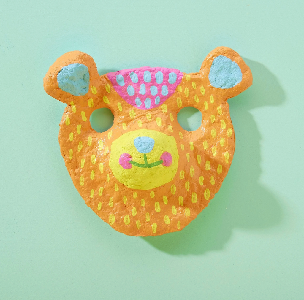 Colorful paper mache animal mask with an orange face that has yellow dots all over it. 