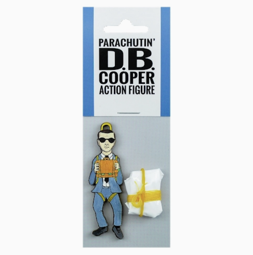Small, clear plastic bag with a die cut figure of a man in a blue suit holding a briefcase strapped to a white parachute folded up. The label reads Parachutin' D.B. Cooper Action Figure.
